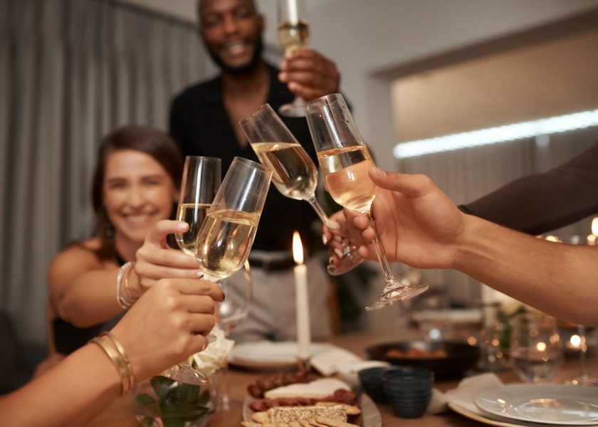 Dinner party, friends and cheers with wine glass for celebration, social gathering or new years event at home. Happy group of people toast alcohol, champagne and drinks to celebrate together at night