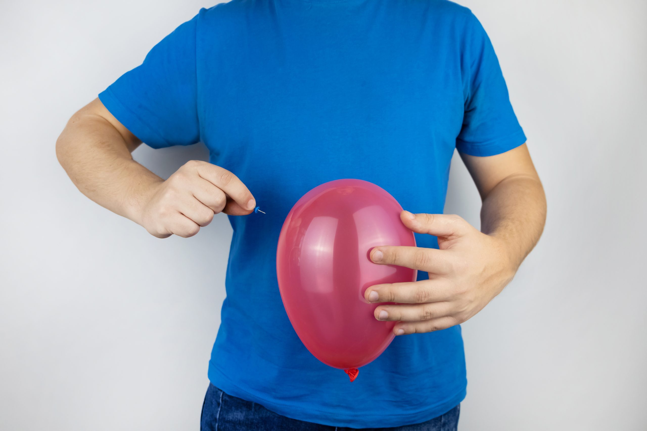 Conceptual photography. The man holds a red ball near his belly, which symbolizes bloating and flatulence. Then he brings a needle to it to burst the balloon and thus get rid of the problem.