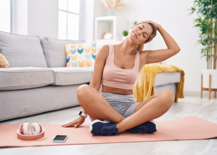 Young blonde woman stretching head sitting on floor at home